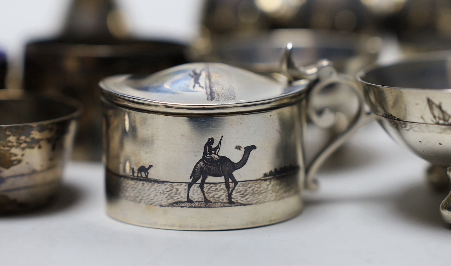 Thirteen assorted Iraq white metal and niello condiments, circular box, five similar napkin rings, a brooch and a pair of similar (damaged) candlesticks.